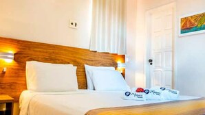 Une chambre d’hôtel avec une tête de lit en bois, du linge de lit blanc et une porte sur laquelle est accrochée une peinture.