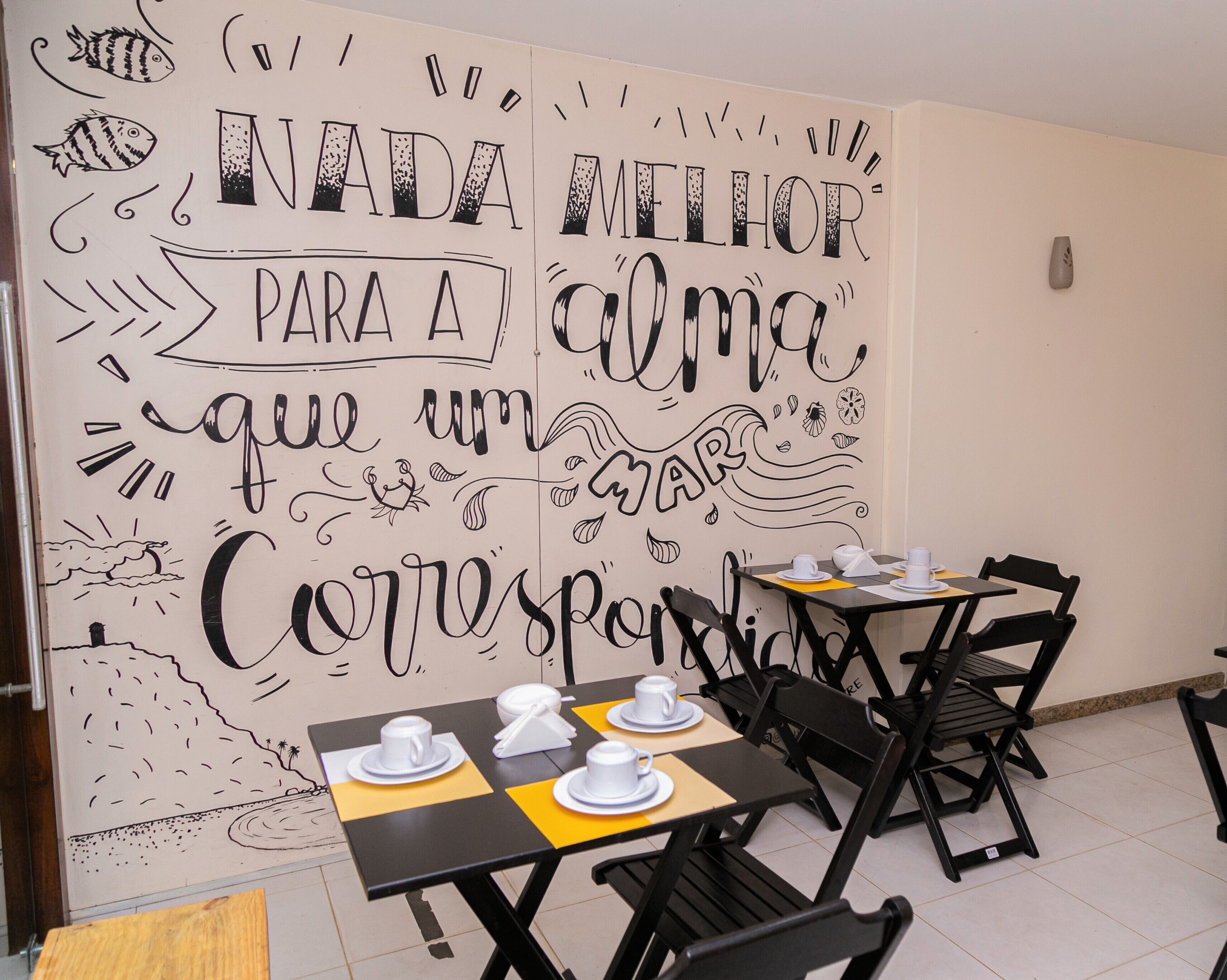 A restaurant interior with tables set for dining, featuring a large wall mural with text and illustrations.