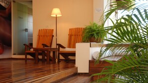 A wooden-floored lobby with a sofa, two chairs, a lamp, and a potted plant.