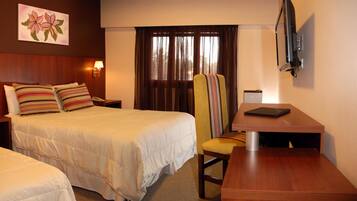 A hotel room with two beds, a desk, a chair, a TV, and a window with curtains.