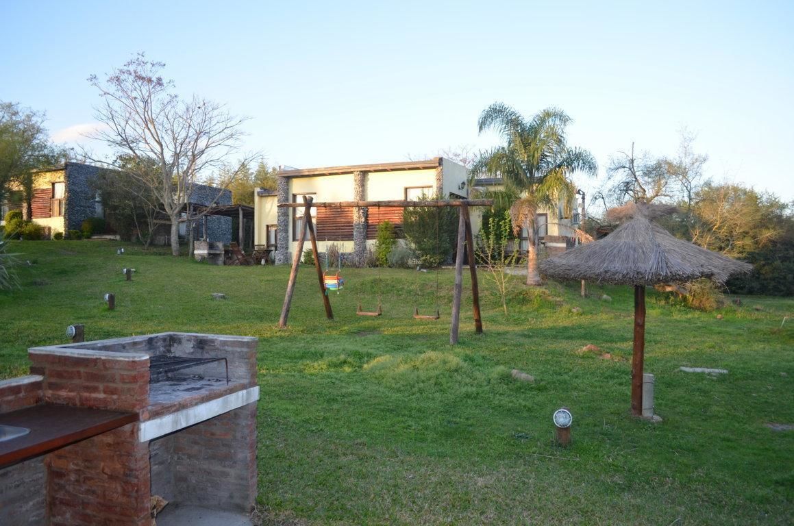 Un patio trasero con una parrilla, columpios y un quiosco cubierto de paja.