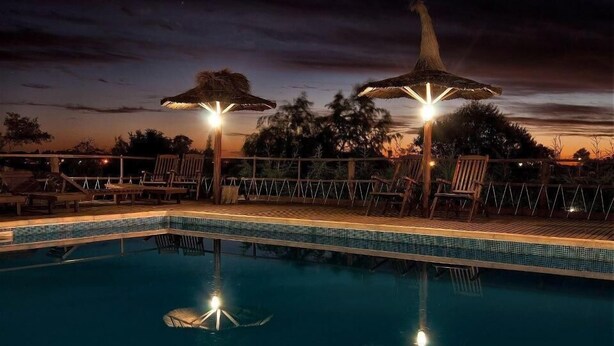 A nighttime pool area with lounge chairs and umbrellas, surrounded by a wooden deck and a pool with clear water. - Terrazas de Colon (Colon)