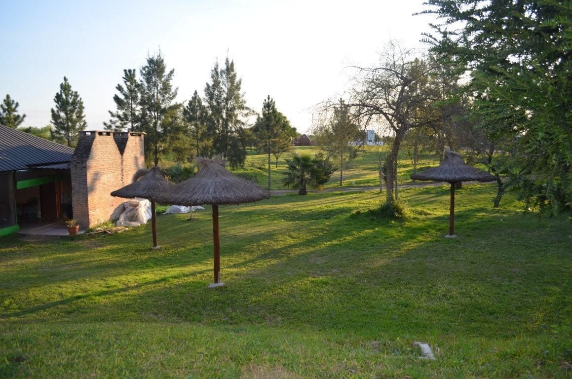 A grassy area with thatched umbrellas and a stone building with a chimney.