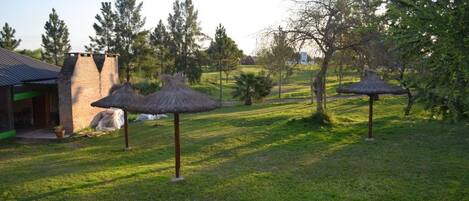 A grassy area with thatched umbrellas and a stone building with a chimney.