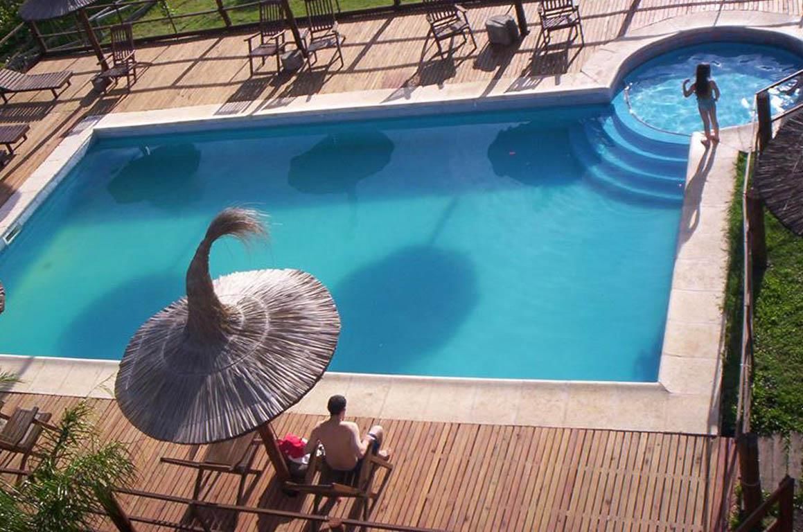 An outdoor swimming pool with a wooden deck, lounge chairs, and a person standing in the water.