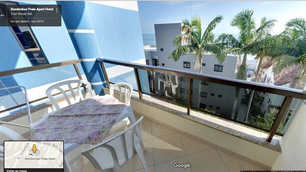 A balcony with a table and chairs, overlooking palm trees and buildings. - Bombinhas Praia Apart Hotel - Unidade Bem Te Vi (Bombinhas)