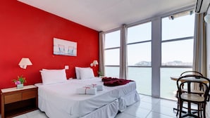 Habitación de hotel con una cama grande, una mesita de noche, una silla y vista al agua.