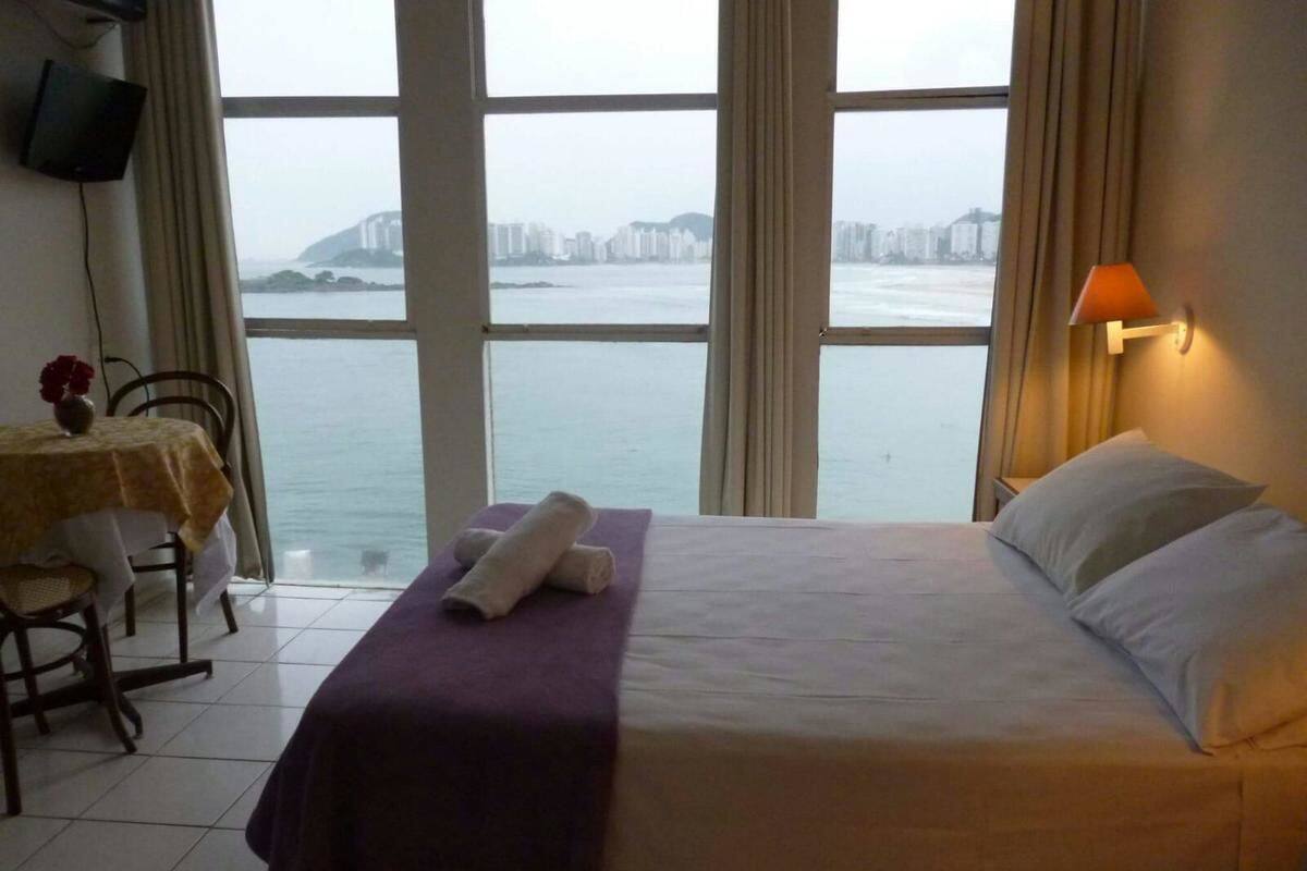 A hotel room with a bed, a table with chairs, a TV, and a view of the city and water.