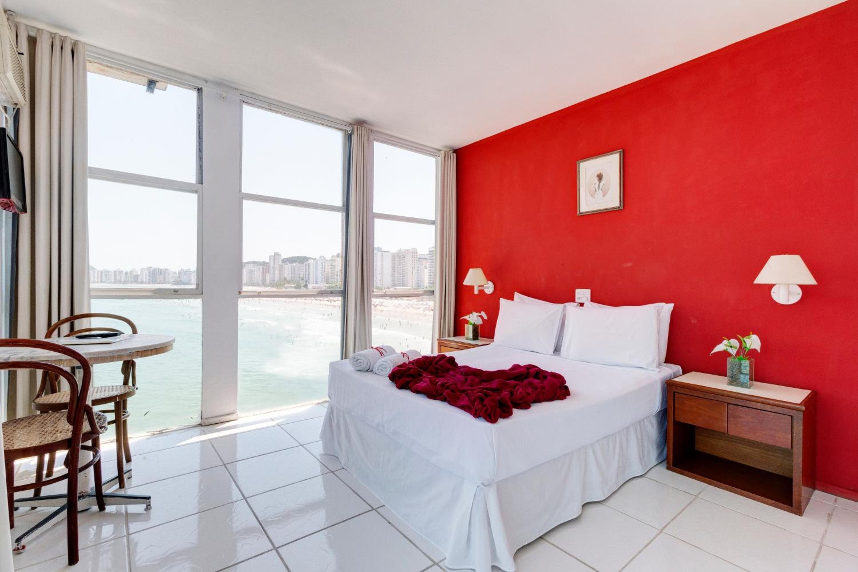 Quarto de hotel com uma cama grande, uma mesa com cadeira e vista para a água.