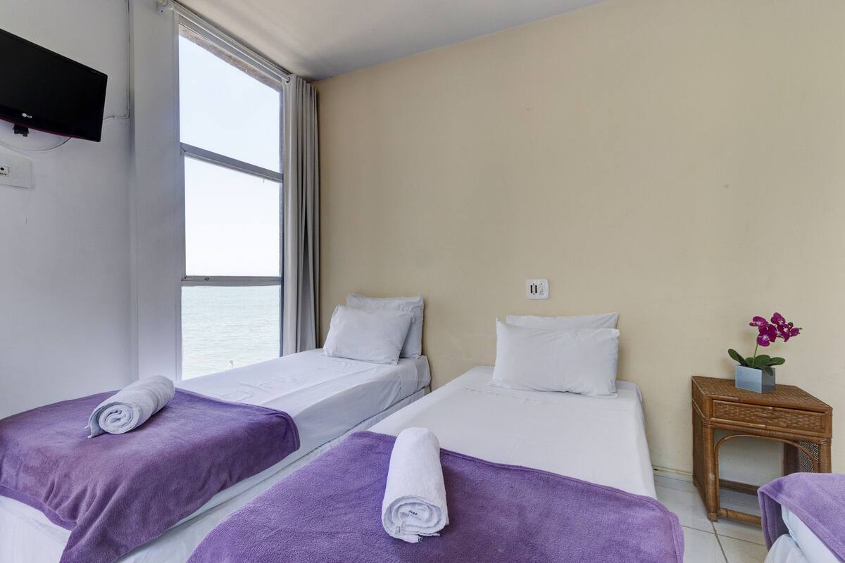 A hotel room with two beds, a window, a TV, and a small wooden side table with a flower.