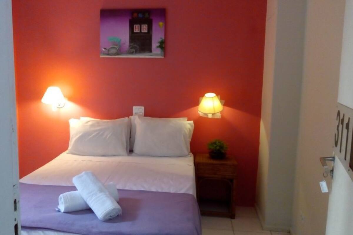 A room with a bed, two wall-mounted lamps, a small table with a plant, and a door.
