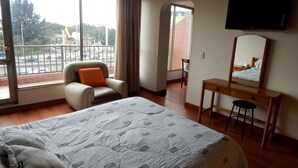 Hotellihuone, jossa on sänky, tuoli, työpöytä, peili ja televisio.