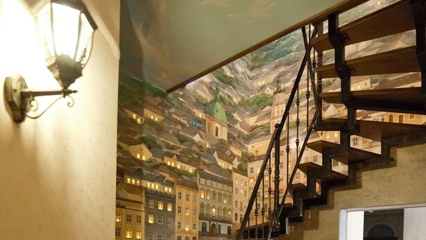 A staircase with wooden steps and metal railings, leading to a room with a tiled floor and a mural on the ceiling depicting buildings. - Guest House Inn Lviv (Lviv)