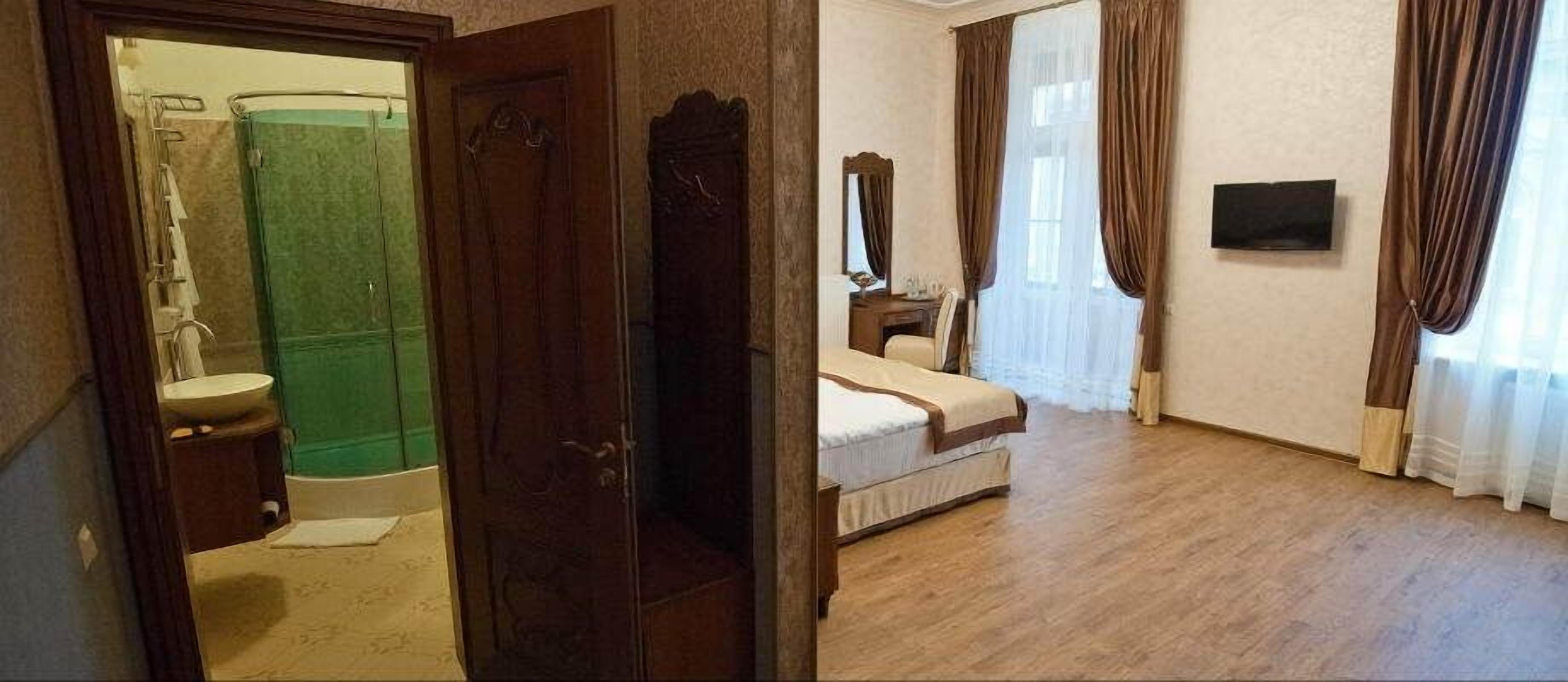 A bathroom with a shower, toilet, and sink. The room has a bed with a headboard, a bedside table, and a TV mounted on the wall.
