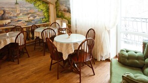 A dining area with wooden tables and chairs, a green sofa, and a mural of a cityscape on the wall. - Guest House Inn Lviv (Lviv)