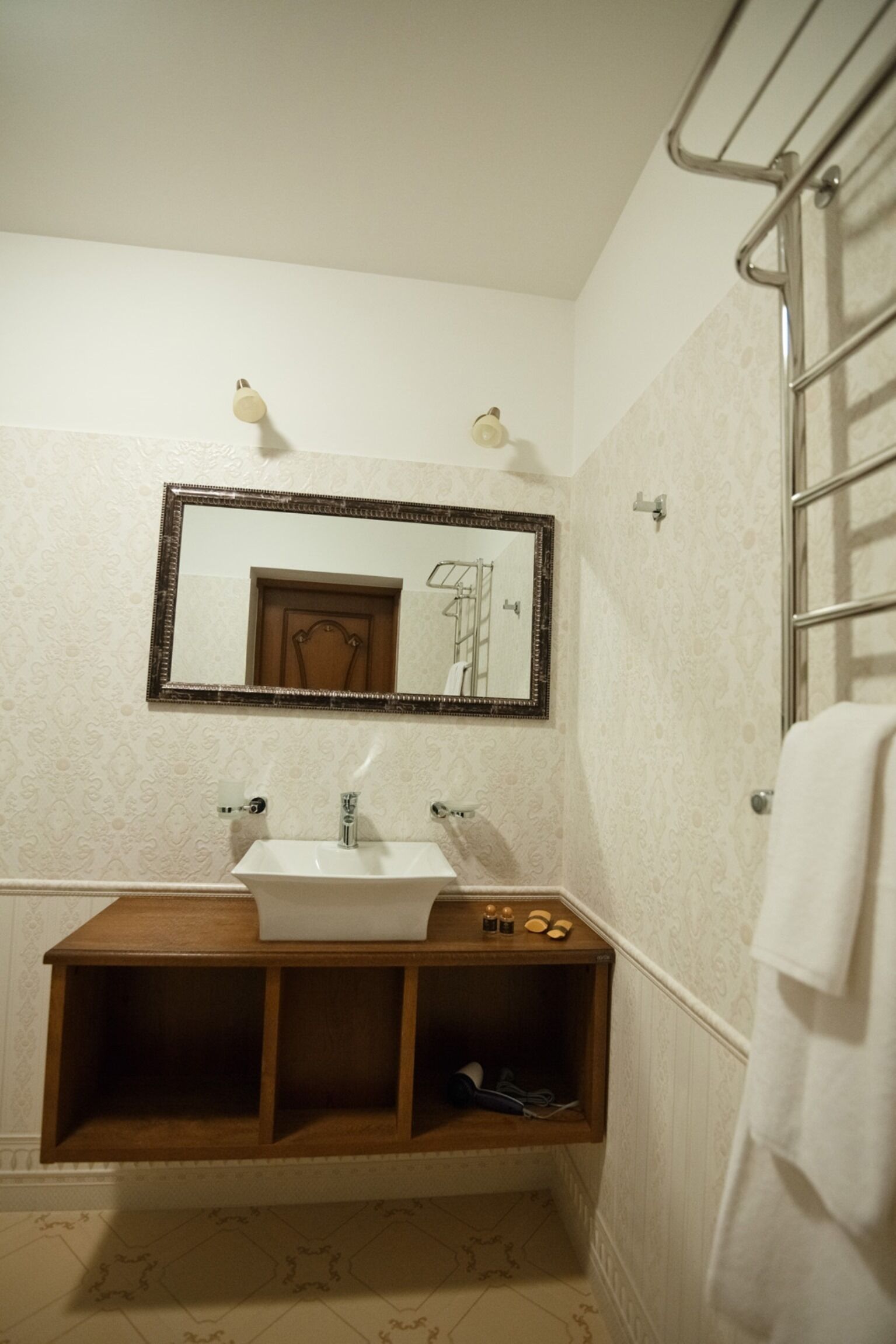 A bathroom with a wooden vanity, a large mirror, and a towel rack.