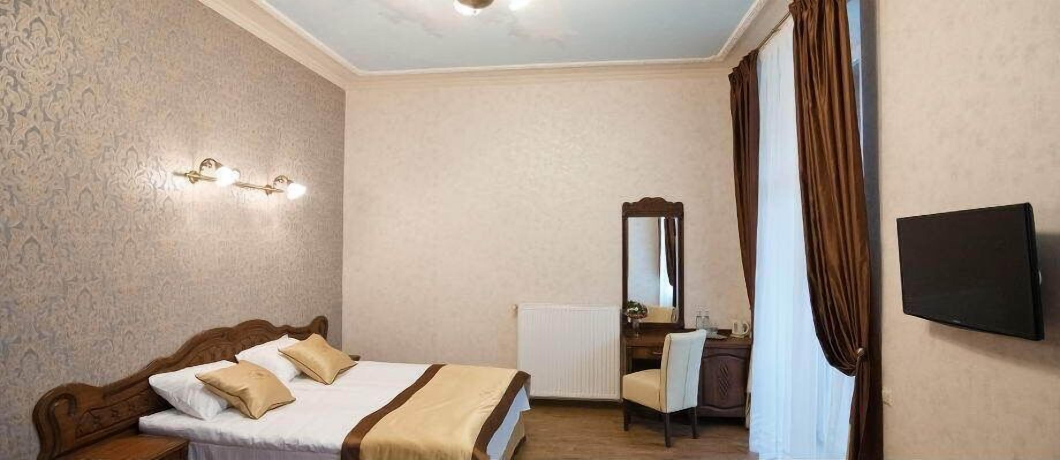 Un dormitorio con cama, escritorio, silla, espejo, radiador y televisor.