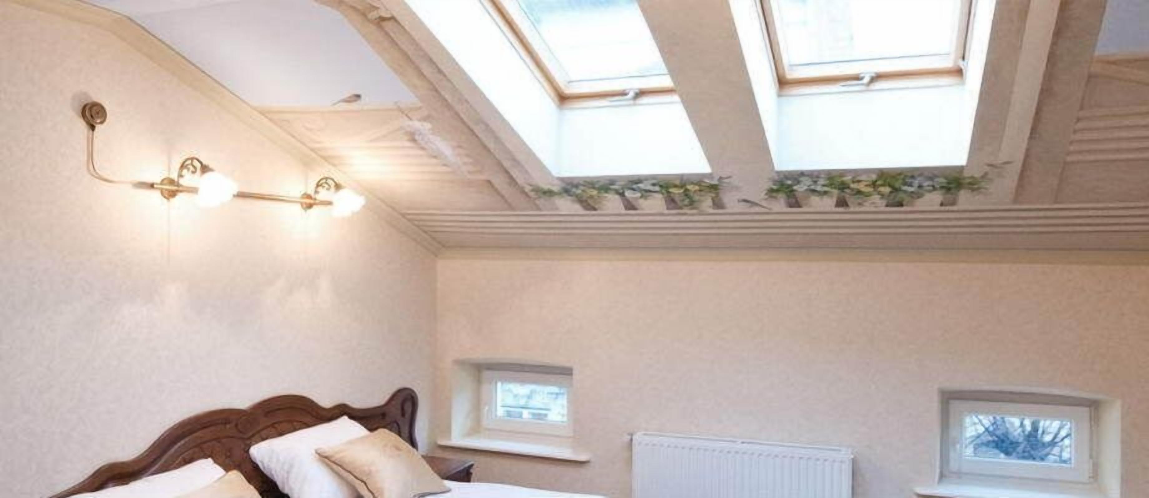 A bedroom with a skylight, a bed, a radiator, and two small windows.
