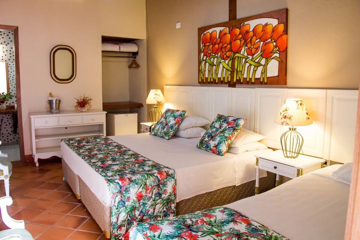 A hotel room with two beds, a dresser, a mirror, and a painting of flowers.