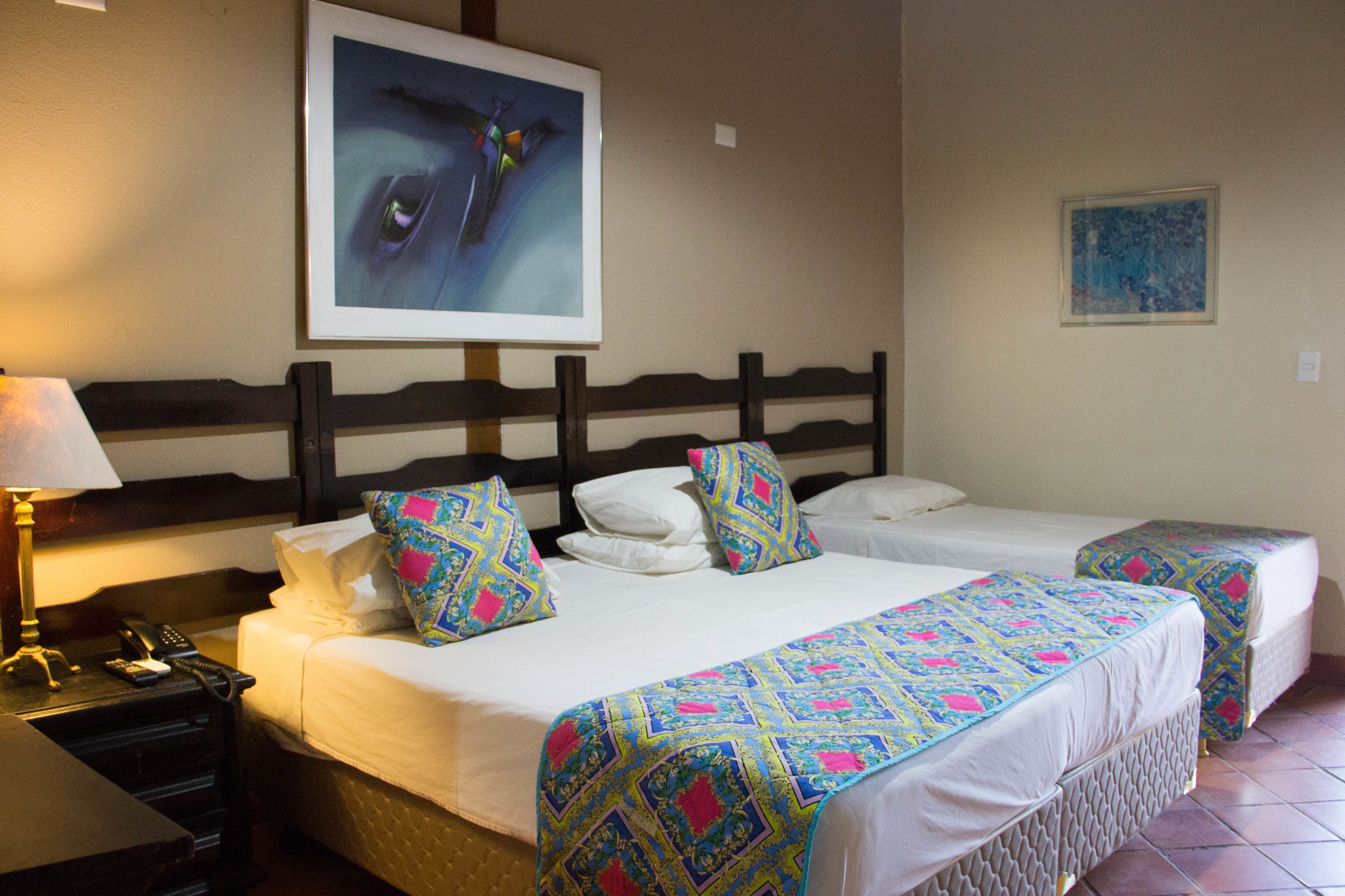 A hotel room with two beds, a nightstand with a lamp, a telephone, and artwork on the walls.