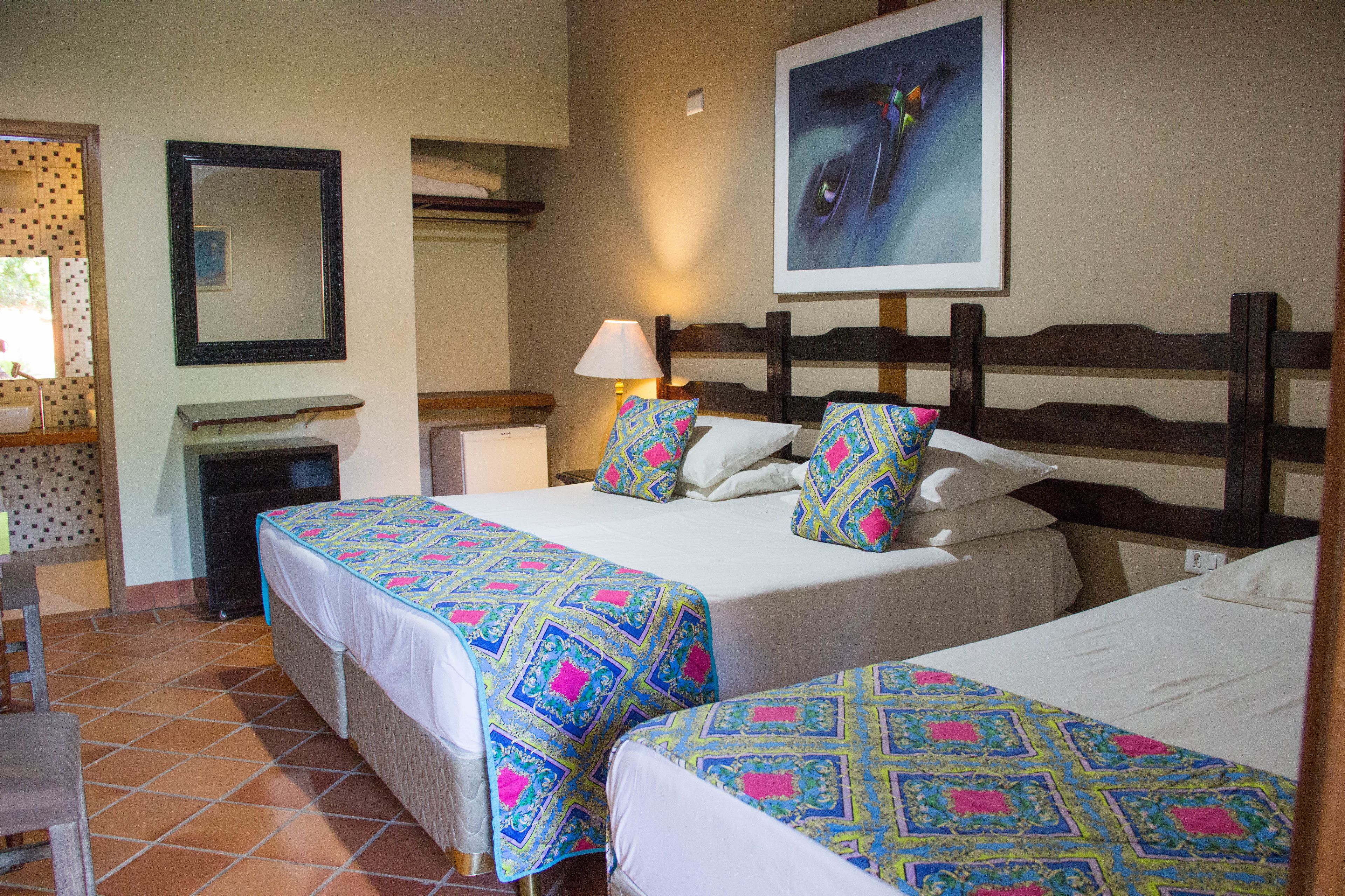 Habitación de hotel con dos camas, una mesita de noche, una lámpara, un espejo y un cuadro en la pared.