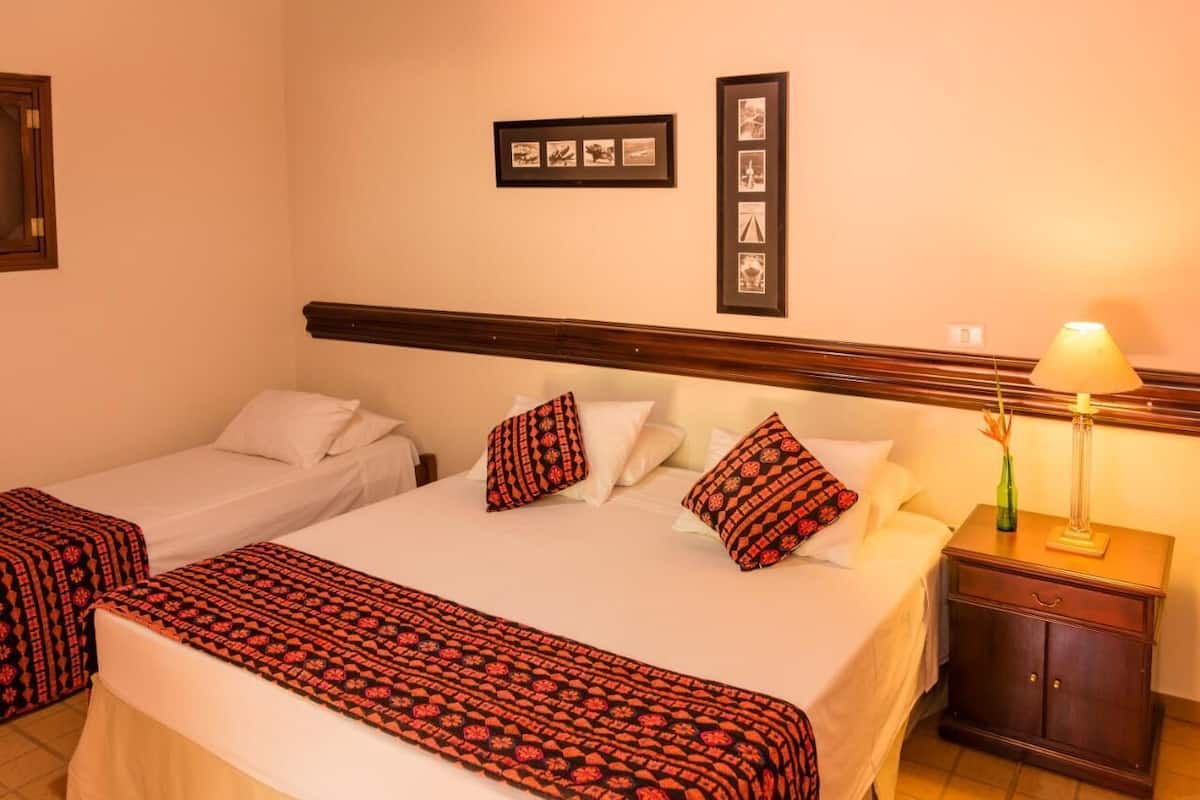 A hotel room with two beds, a nightstand, and a lamp. There are framed pictures on the wall.