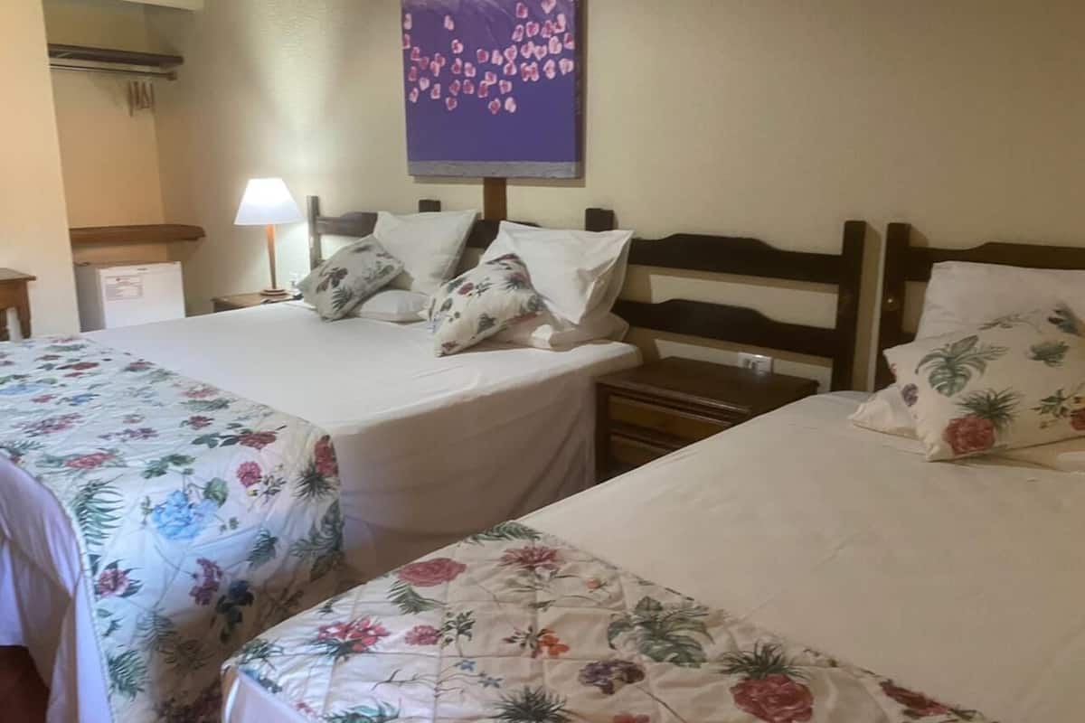A hotel room with two beds, each with floral bedding and white pillows. There is a nightstand with a lamp between the beds.