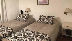 A hotel room with two beds, each with patterned bedding, a bedside table with a lamp, a framed picture on the wall, and a pair of shoes on the floor. - Hotel Bariloche Flat (Bariloche)