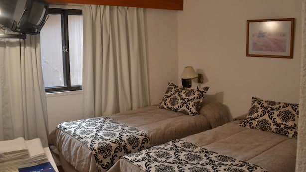 A room with two beds, a window with curtains, a lamp, and a framed picture on the wall. - Hotel Bariloche Flat (Bariloche)