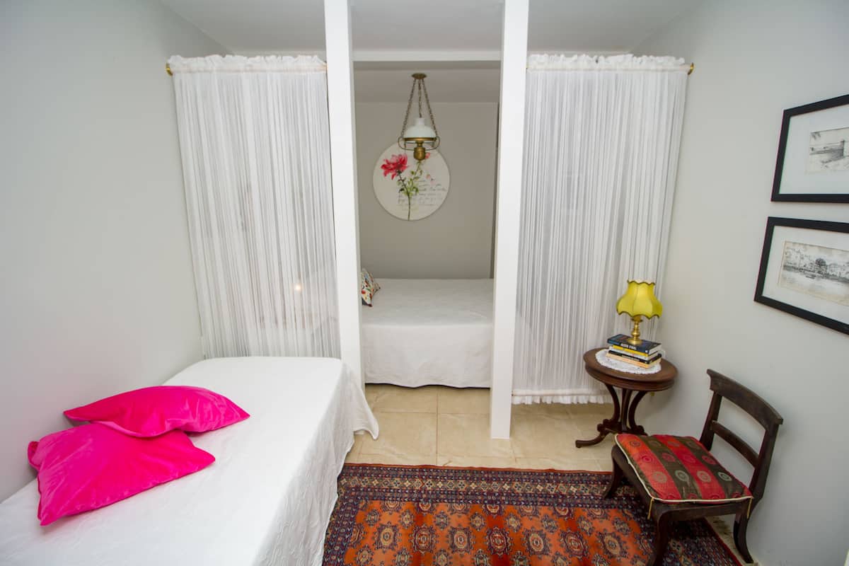 A bedroom with a bed, two pillows, a nightstand, a chair, a lamp, and a framed picture on the wall.
