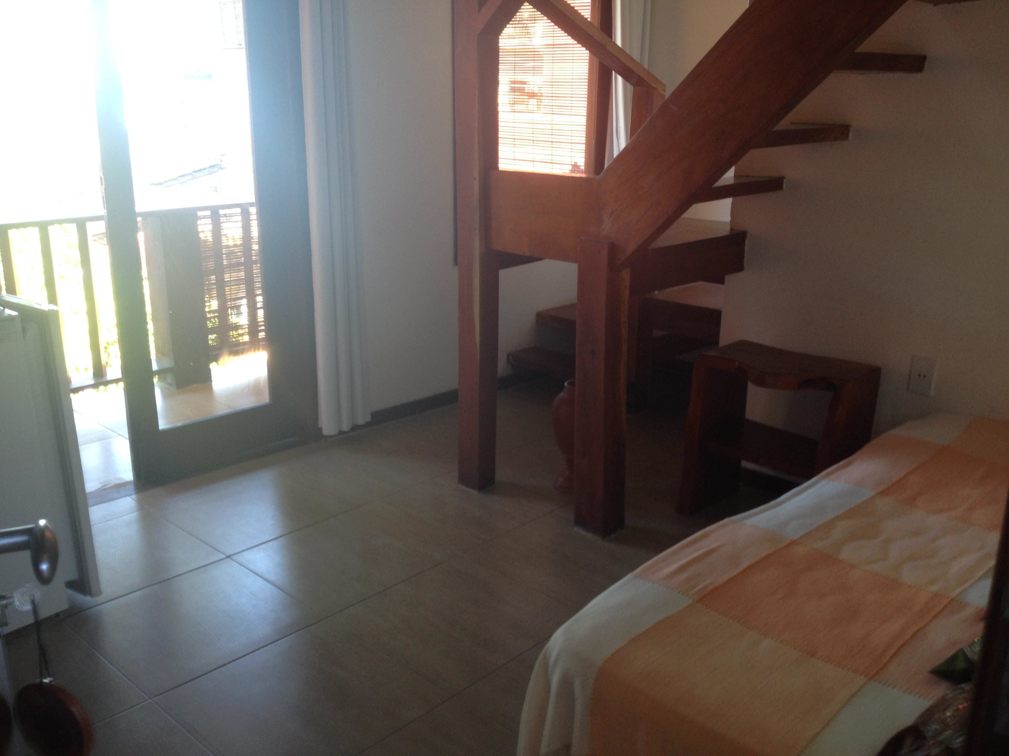 A bedroom with a bed, a wooden staircase, a door, and a window.