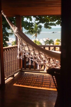 Un hamac sur un balcon en bois, avec vue sur l’océan et les palmiers.