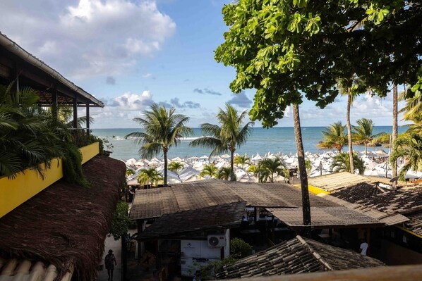 A beach view with a thatched-roof building, palm trees, and beach umbrellas.