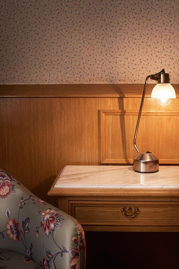 A wooden headboard with a floral-patterned wallpaper, a desk with a lamp, and a floral-patterned sofa. - Gran Hotel Ailen (Buenos Aires)