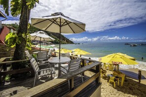 Un restaurante frente a la playa con terraza, mesas y sillas, y sombrillas amarillas.