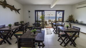 Un comedor con mesas y sillas de madera, una decoración de pescado grande en la pared, y vista al mar a través de amplias ventanas.