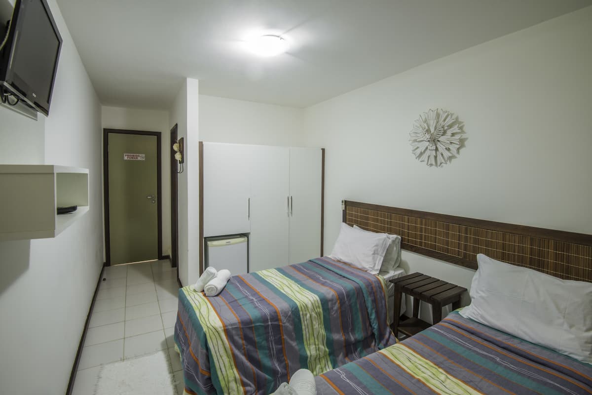 Quarto de hotel com duas camas, televisão, uma mesinha e um objeto decorativo na parede.