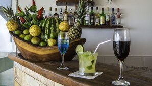 Una zona de bar con un mostrador de madera, un cuenco de frutas y tres vasos de bebidas variadas.