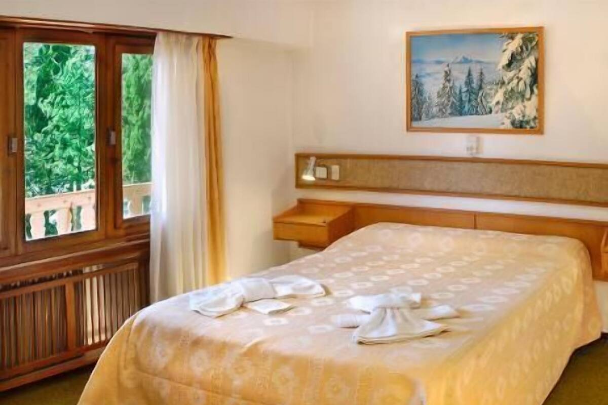 A hotel room with a bed, a painting on the wall, and a window with curtains.