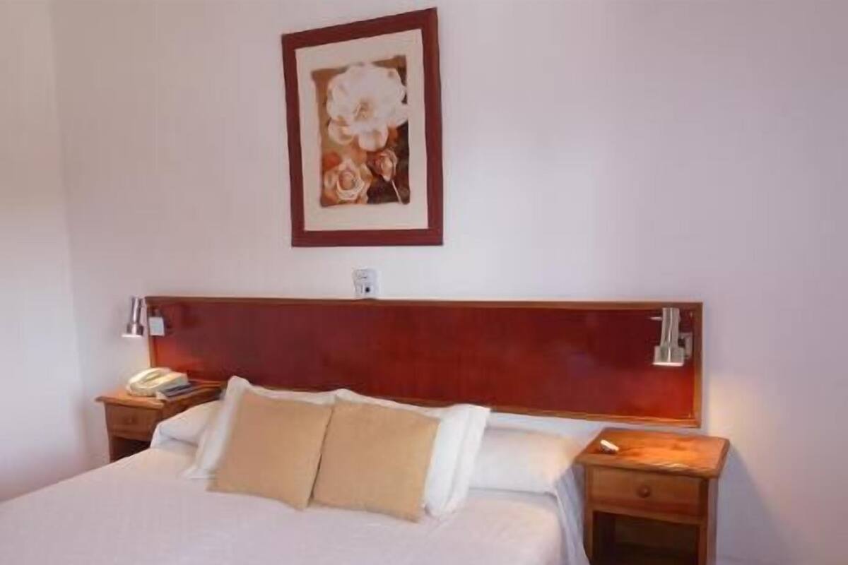 A hotel room with a large bed, two bedside tables, a nightstand, and a framed picture on the wall.