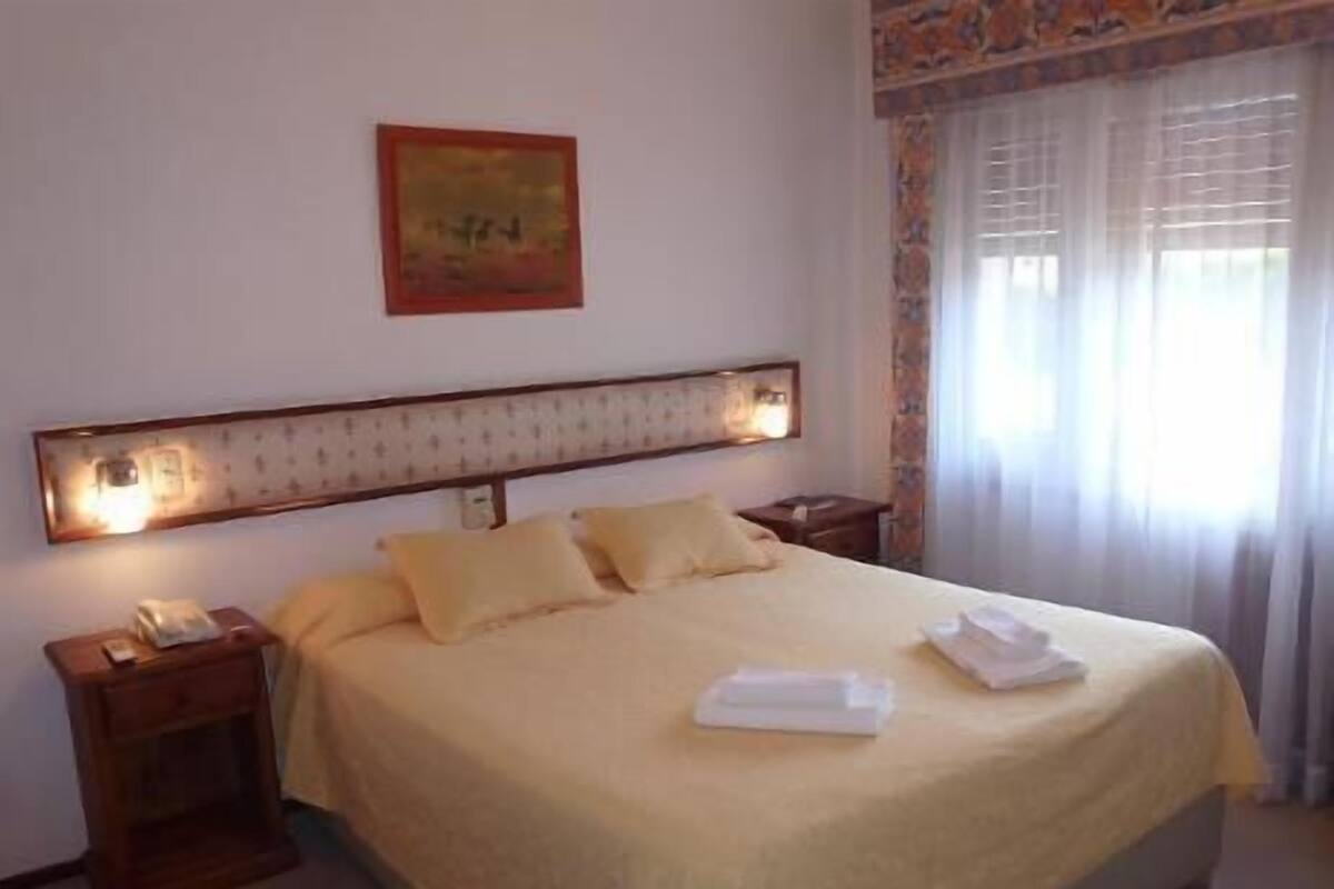 A hotel room with a large bed, a nightstand, a telephone, and a painting on the wall.