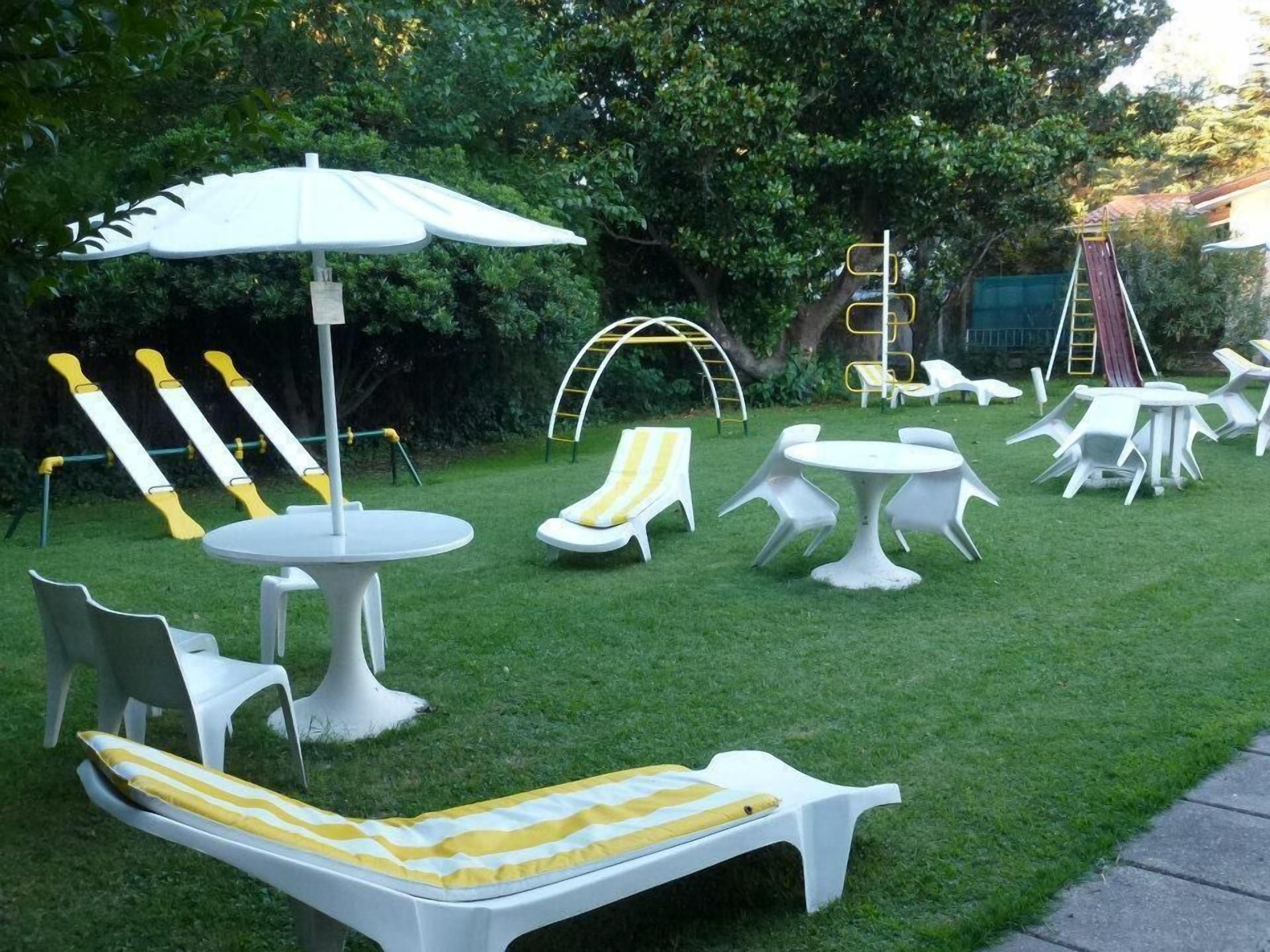Un jardín con sillones blancos, una mesa y un banco a rayas amarillas.