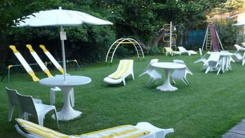 Un jardín con sillones blancos, una mesa y un banco a rayas amarillas.