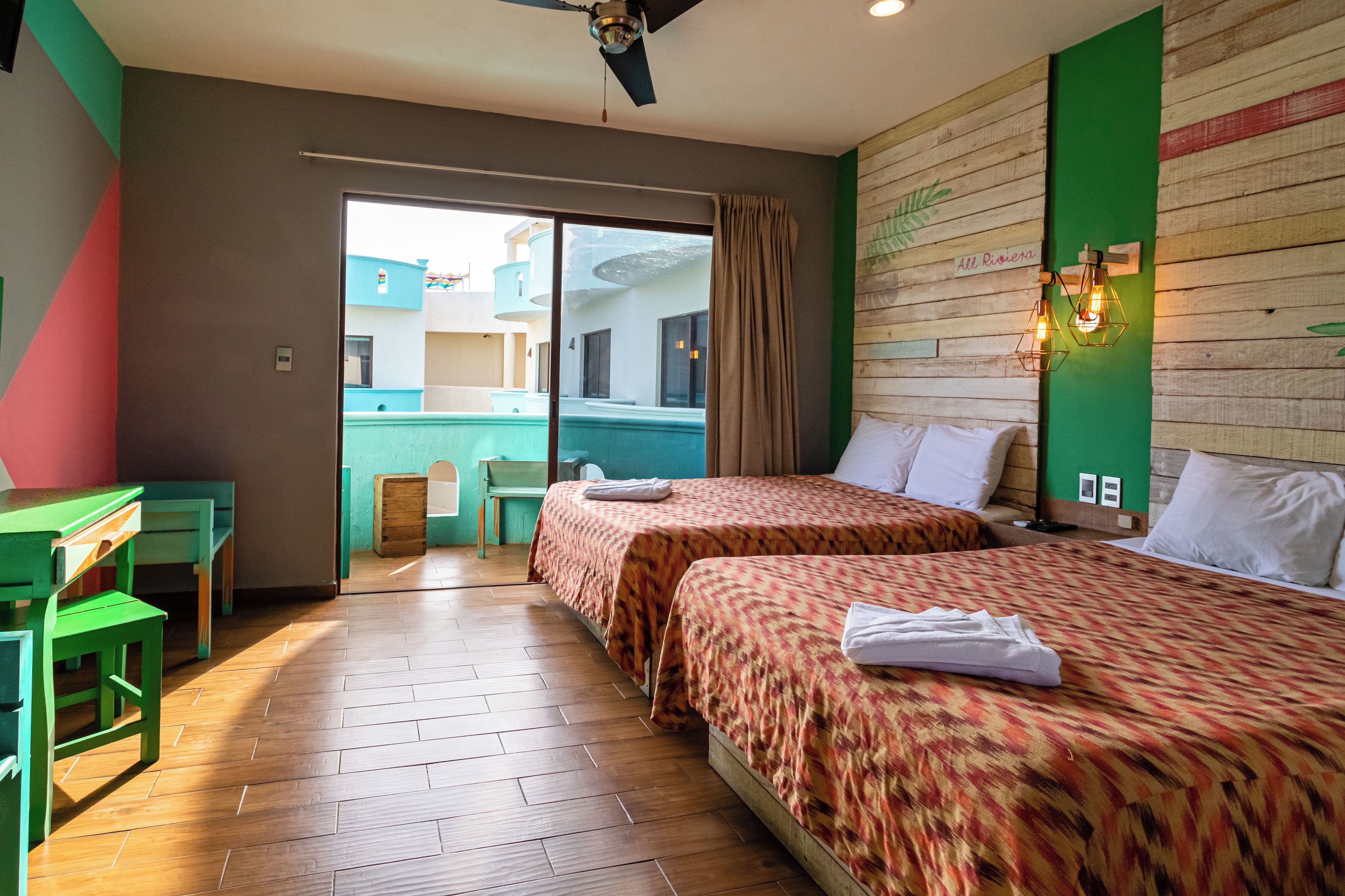 A hotel room with two beds, a desk, a chair, and a view of a building outside.