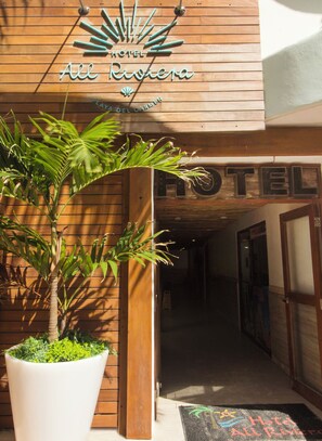 A hotel entrance with a wooden facade, a potted plant, and a doormat with the hotel's name. - All Riviera (Playa del Carmen)