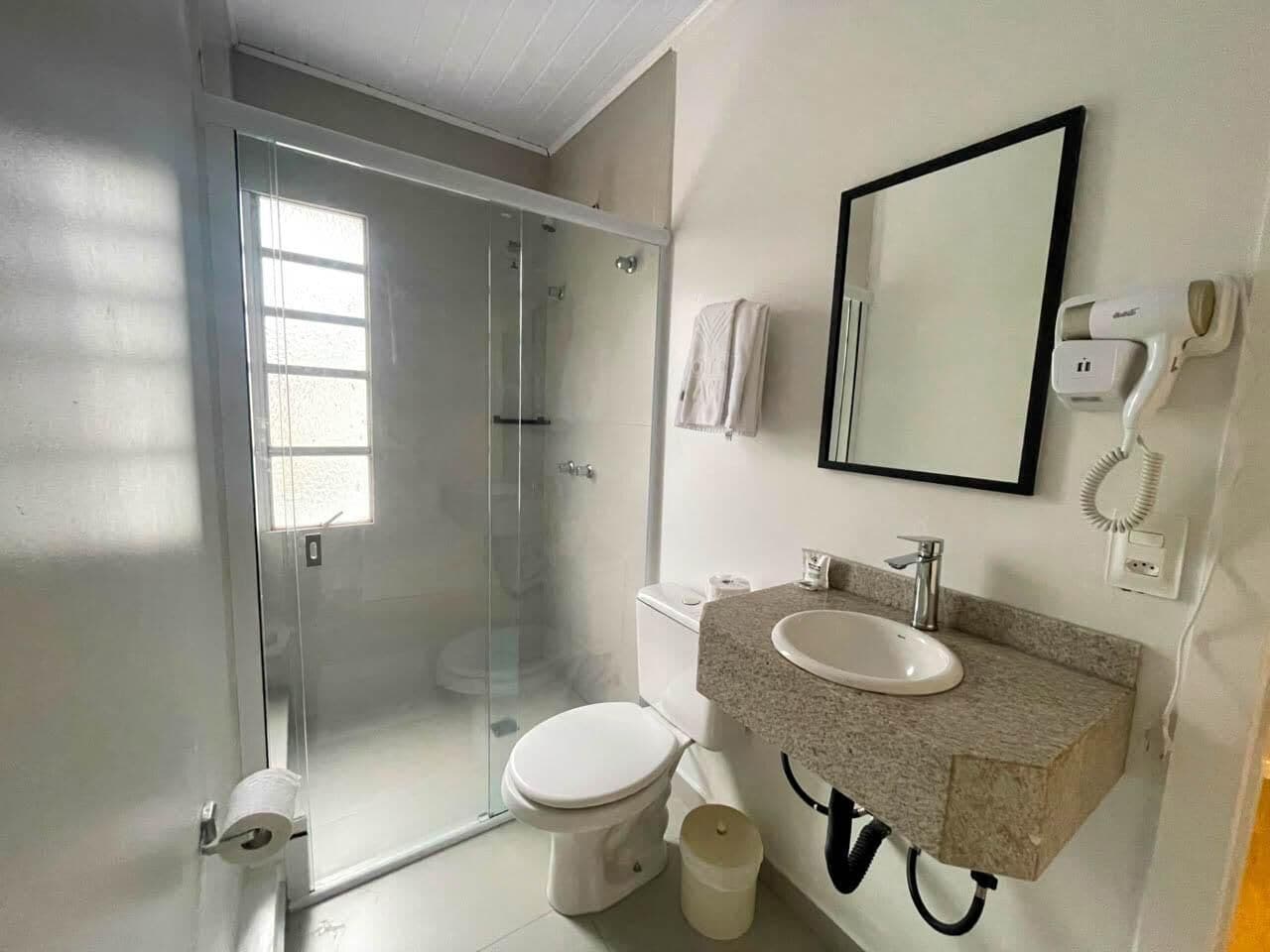 A bathroom with a glass-enclosed shower, a toilet, a sink with a mirror, and a towel hanging on the wall.