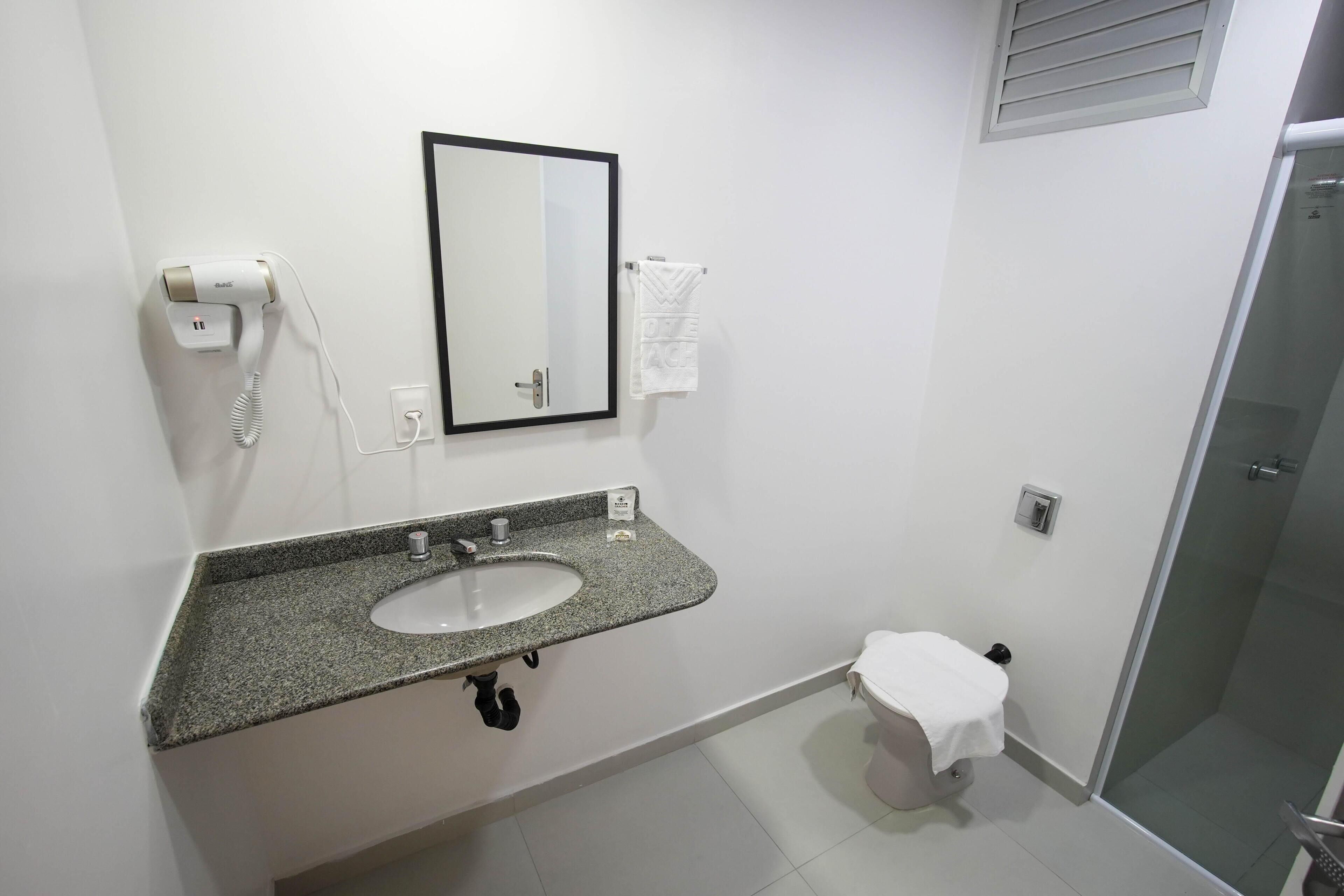 Un baño con lavamanos de encimera de granito, un espejo, inodoro y zona de ducha.
