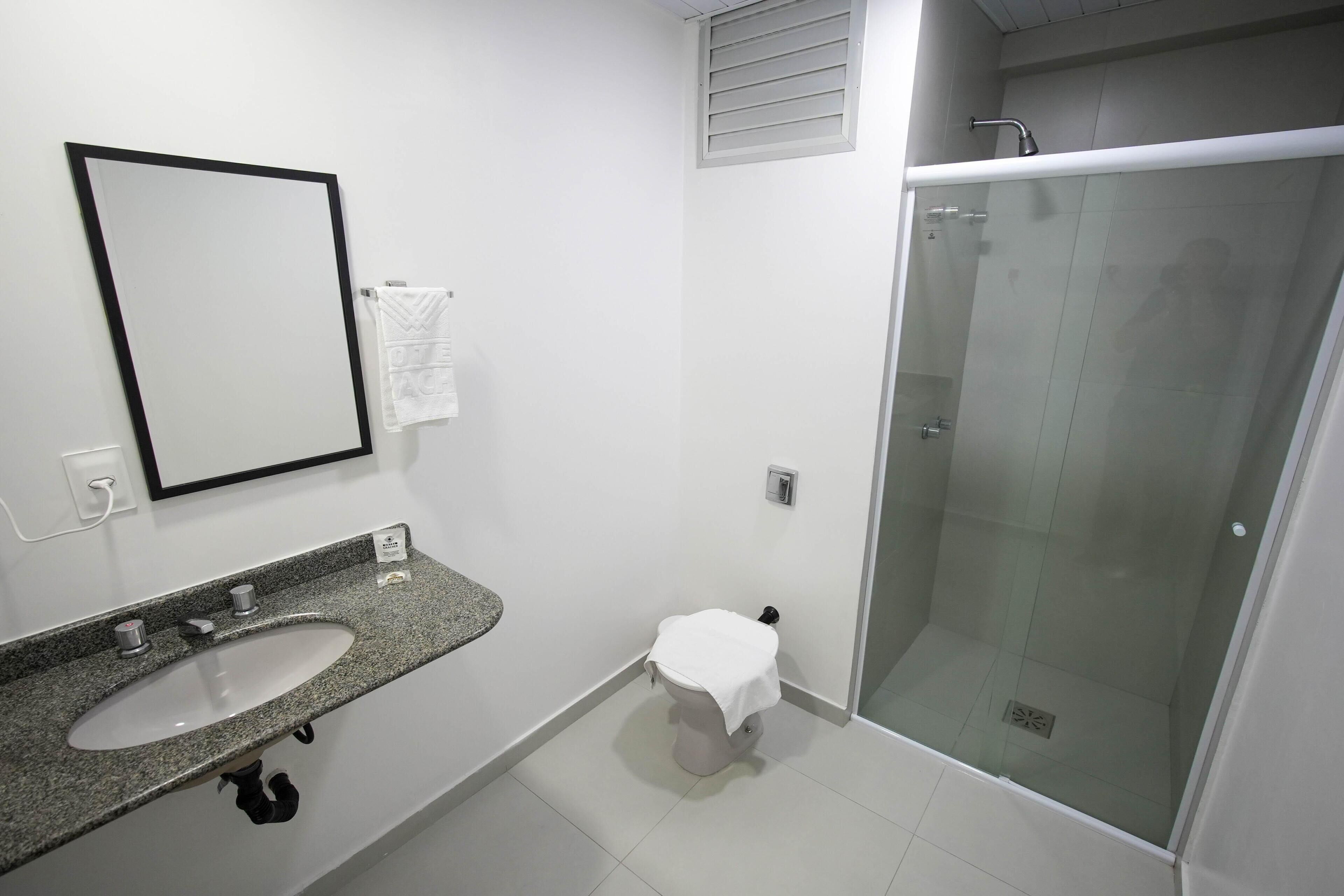 Un baño moderno con lavamanos de granito, un inodoro pequeño y una ducha con cerramiento de vidrio.