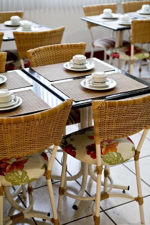 Un restaurante con sillas y mesas de mimbre, algunas con platos y tazas.