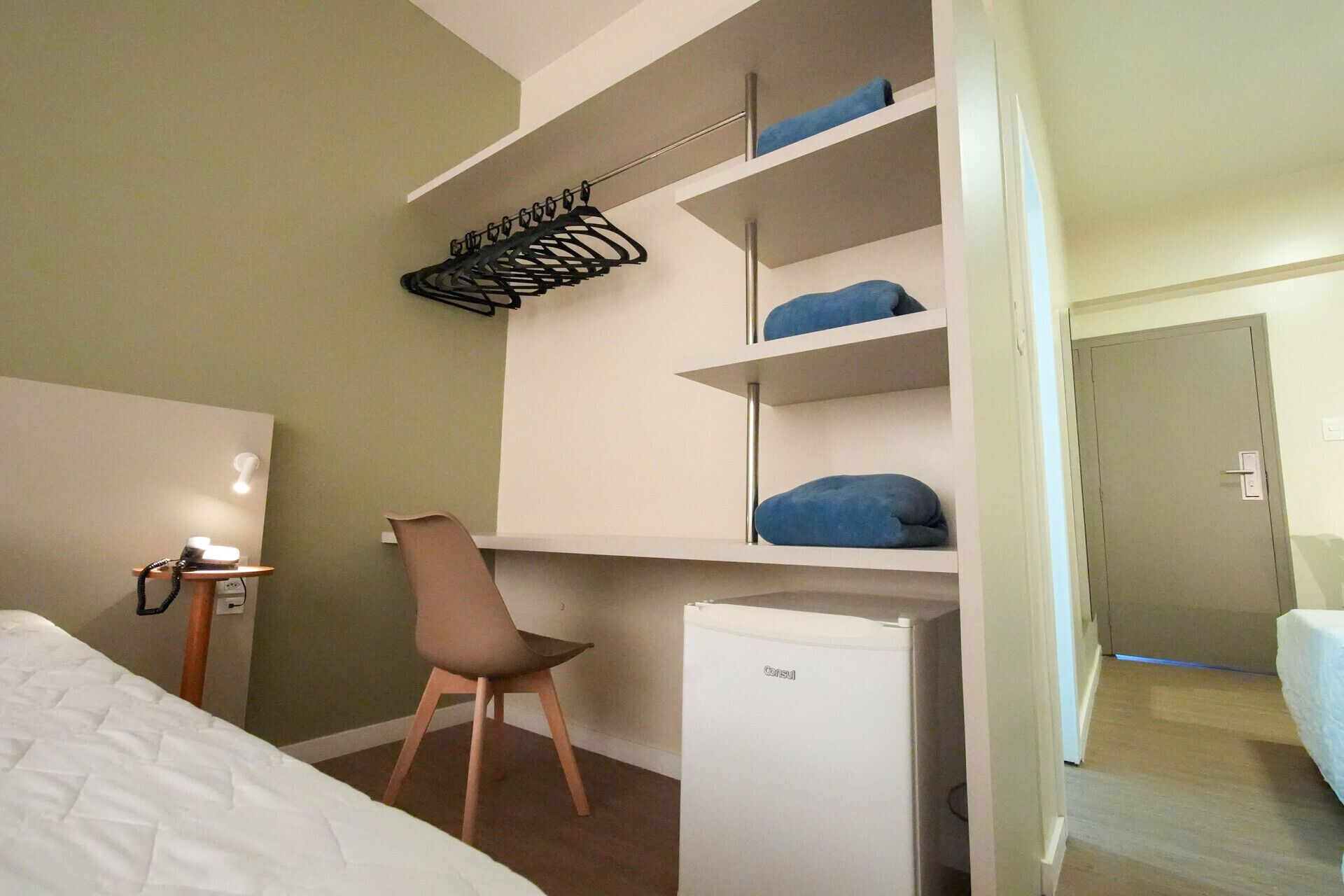 Une chambre d’hôtel équipée d’un lit, d’un bureau, d’une chaise, d’une armoire et d’un petit réfrigérateur.